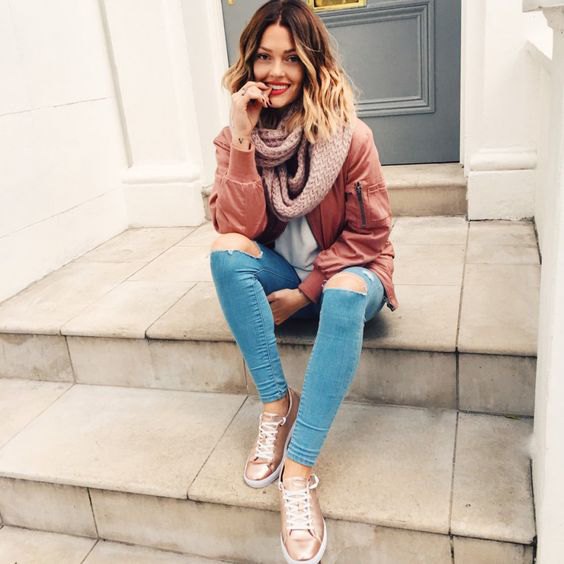 blushing pink bomber jacket with light blue skinny jeans and gold sneakers