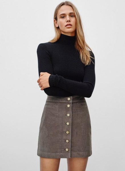 black, figure-hugging sweater with stand-up collar and gray, high-waisted mini cord skirt