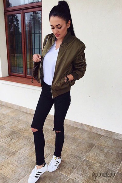 olive bomber jacket with white v-neck blouse and black ripped jeans