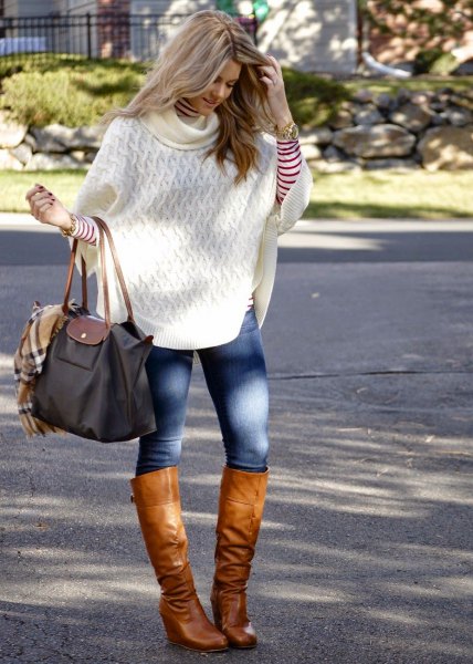 white knitted poncho shirt with blue skinny jeans and knee-high boots in brown leather